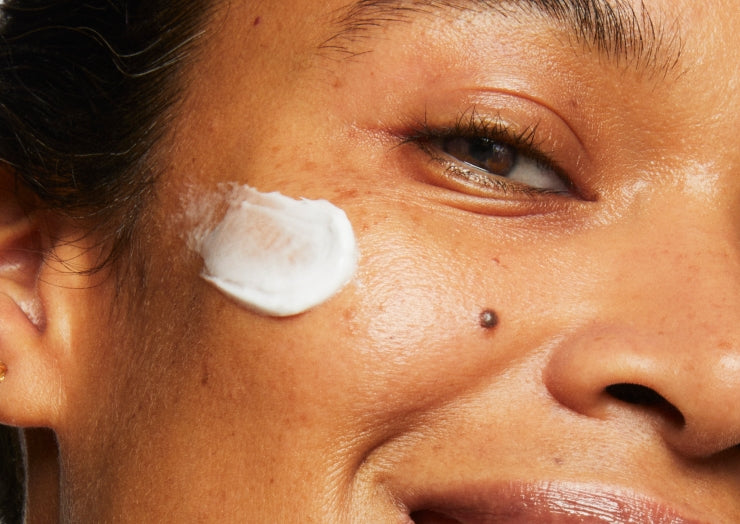 Close-up portrait of a model smiling. They are wearing a swipe of Milk Makeup Vegan Milk Moisturizer on their face.